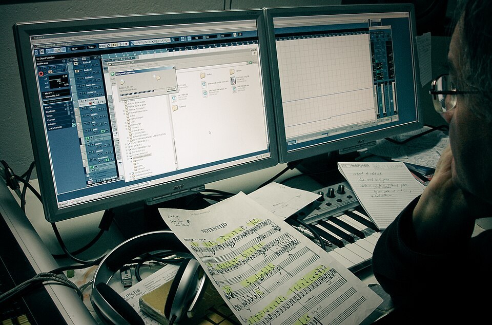 2台のモニターにCubaseを表示し、手書きの書き込みがある楽譜とMIDIキーボードを前に作業する人