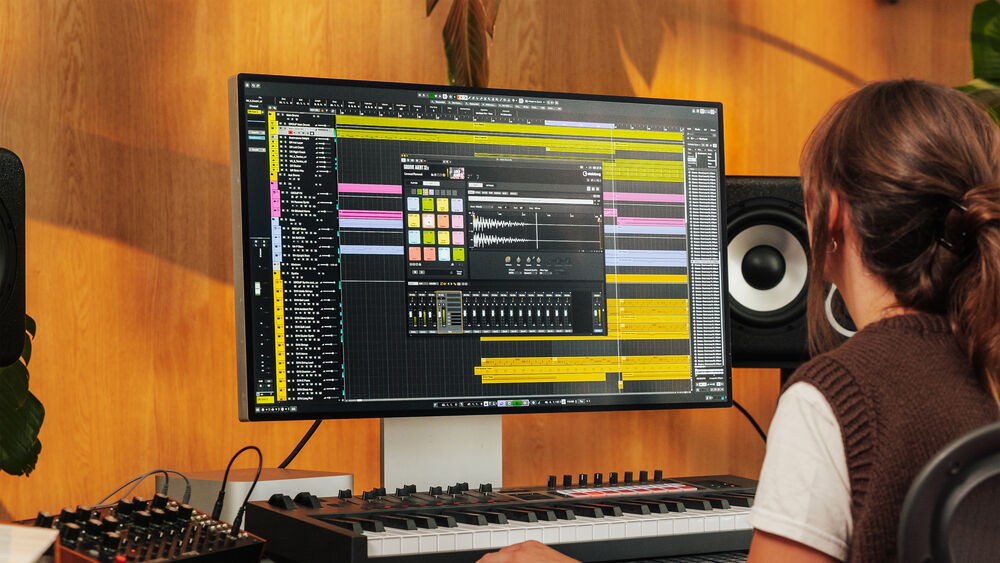 大きなモニターにCubase 15のプロジェクト画面を表示し、MIDIキーボードの前で作業する女性